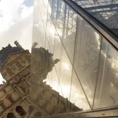 Piramide Luwru i zabytkowy budynek odbijające się w szkle.