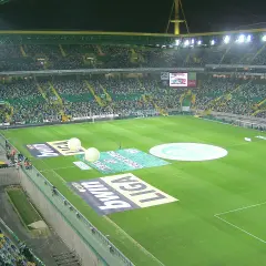 Widok na pełen widzów **sporting lizbona stadion** przed meczem. Na murawie widoczne są logotypy sponsorów i wielkie balony.