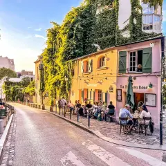Ulica Montmartre w Paryżu z kawiarnią La Maison Rose i ludźmi siedzącymi przy stolikach.