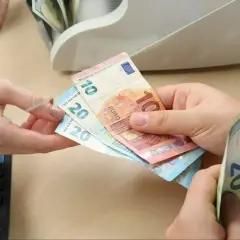 Dłonie przekazujące banknoty euro (10 i 20 euro) obok banknotów i licznika pieniędzy.