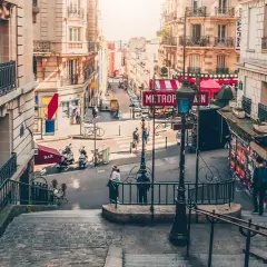 Schody prowadzące do paryskiej ulicy z szyldem "METROPOLITAIN" i budynkami w stylu Haussmanna.