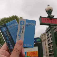 Dłoń trzyma paryskie karty Navigo na tle znaku metra.