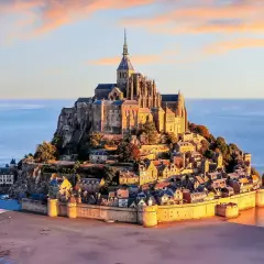 Opactwo Mont Saint-Michel na skalistej wyspie otoczonej wodą, o zachodzie słońca.