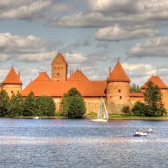 Malowniczy zamek na Litwie, otoczony wodą, z żaglówką i łódkami na jeziorze.