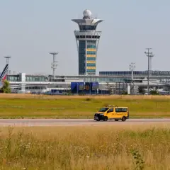 Żółty van z napisem "INSPECTION" na tle lotniska z wieżą kontroli lotów i samolotami.