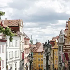 Ulica w Pradze z zabytkowymi kamienicami i latarniami. W oddali widać wieże, wskazujące na praga nietypowe atrakcje.