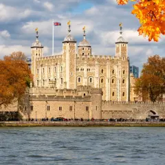 Jesienna panorama Londynu z twierdzą Tower i rzeką Tamizą. Liście drzew mienią się złotem.