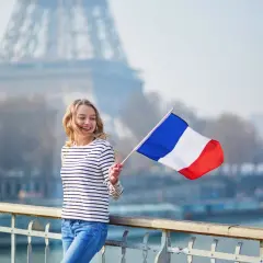 Uśmiechnięta kobieta z flagą Francji na tle wieży Eiffla.