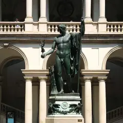 Wielki posąg w centrum dziedzińca Pinacoteca. Nad nim arkady i balustrada, z której obserwują ludzie.