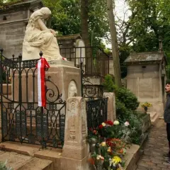 Pomnik na cmentarzu Père Lachaise z biało-czerwoną wstęgą. Mężczyzna wpatruje się w nagrobek.