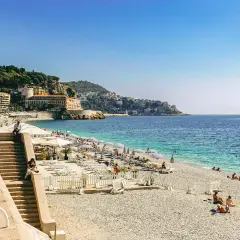Kamienista plaża w Nicei z leżakami, parasolami i turystami.