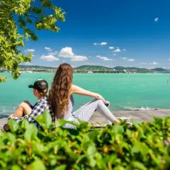 Dzieci odpoczywają na plaży Balaton, podziwiając turkusową wodę i zielone wzgórza w oddali.