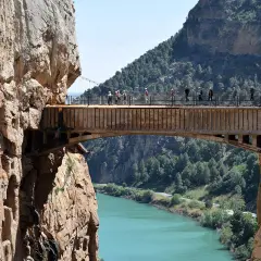 Spacerzy po wąwozie El Caminito del Rey, atrakcji, z której słynie Malaga. Widok na most nad turkusową rzeką.