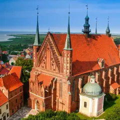 Widok na Frombork z zamkiem i katedrą. Czerwone dachy budowli kontrastują z błękitem nieba i zielenią otoczenia.