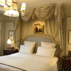 Elegancka sypialnia w hotelu Ritz w Paryżu, z baldachimem nad łóżkiem, kryształowym żyrandolem i zabytkowymi obrazami.