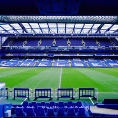 Puste trybuny stadionu Chelsea Londyn, zielona murawa i niebieskie siedzenia czekają na kibiców.