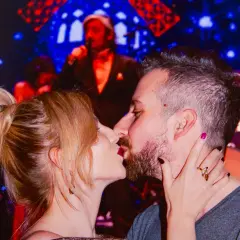 Para całująca się na tle sceny z muzykiem i światłami.