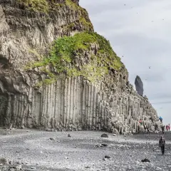 Niesamowita czarna plaża Islandia z bazaltowymi kolumnami i jaskinią. Turyści spacerują po kamieniach.