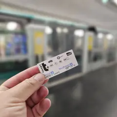 Dłoń trzyma bilet metra paryskiego na tle pociągu.