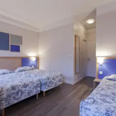 Pokój hotelowy z trzema łóżkami w niebiesko-białą pościelą i niebieskimi zagłówkami.