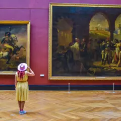 Kobieta w różowym kapeluszu podziwia obrazy w najwiekszym muzeum świata.