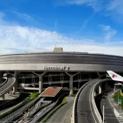 Terminal 1 na lotniskach w Paryżu, z charakterystyczną, okrągłą architekturą i drogami prowadzącymi do niego. Widoczny fragment skrzydła samolotu Qatar Airways.