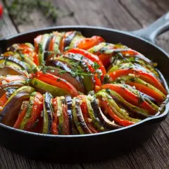 Ratatouille, jedno z popularnych dań francuskich, w naczyniu żeliwnym. Warzywa ułożone w wachlarz, ozdobione ziołami.