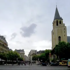 Wieża kościoła Saint-Germain-des-Prés na tle paryskiej ulicy z budynkami i przechodniami.