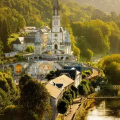 Bazylika w Lourdes, francuskie ośrodek kultu maryjnego, w otoczeniu zielonych wzgórz i rzeki.