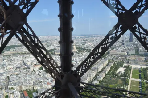 Widok z tarasu widokowego Wieży Eiffla na Paryż. Metalowa konstrukcja wieży tworzy ramę dla rozległej panoramy miasta.