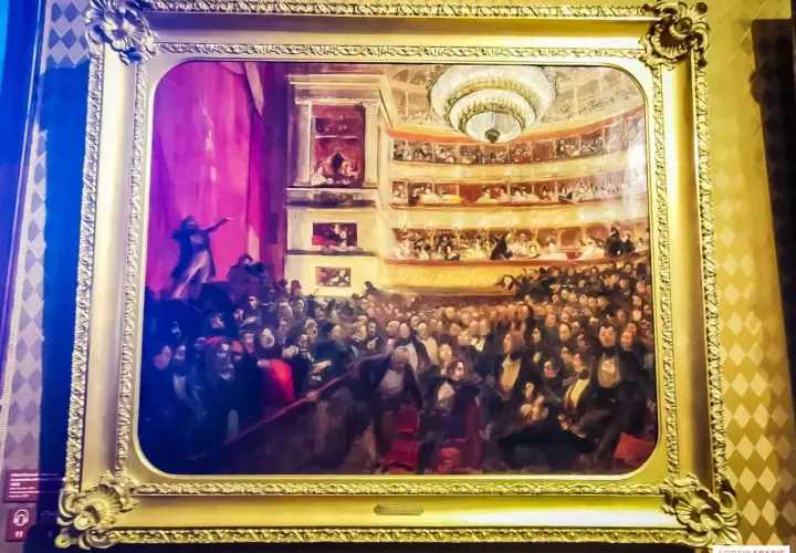 Obraz przedstawia tłum w teatrze, być może inspirowany **najważniejszymi dziełami Victora Hugo**, z widownią i lożami.