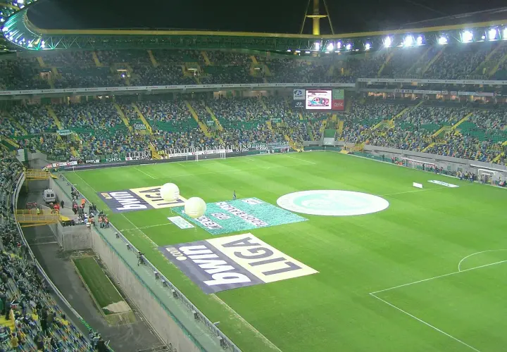 Widok na pełen widzów **sporting lizbona stadion** przed meczem. Na murawie widoczne są logotypy sponsorów i wielkie balony.