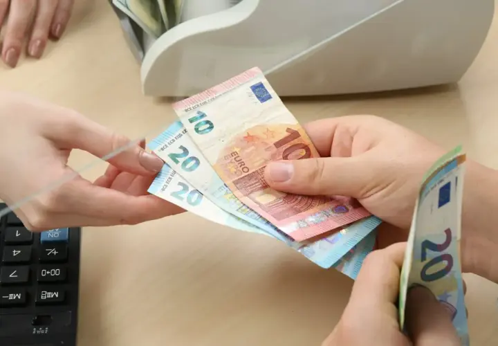 Dłonie przekazujące banknoty euro (10 i 20 euro) obok banknotów i licznika pieniędzy.