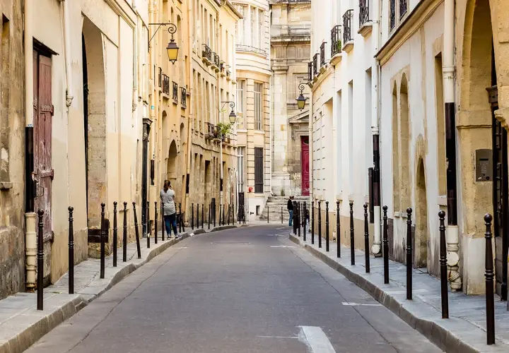 Urokliwa uliczka w paryskiej dzielnicy Le Marais, z kamiennymi budynkami i latarniami.