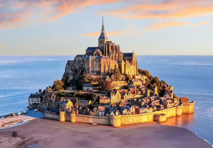 Opactwo Mont Saint-Michel na skalistej wyspie otoczonej wodą, o zachodzie słońca.