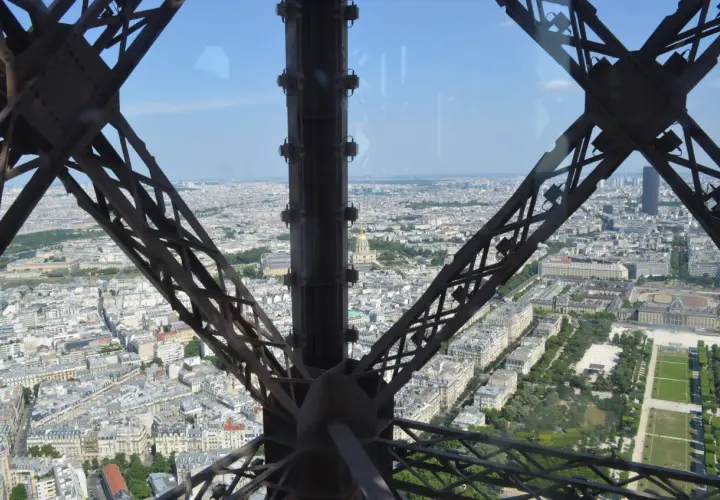 Widok z tarasu widokowego Wieży Eiffla na Paryż. Metalowa konstrukcja wieży tworzy ramę dla rozległej panoramy miasta.