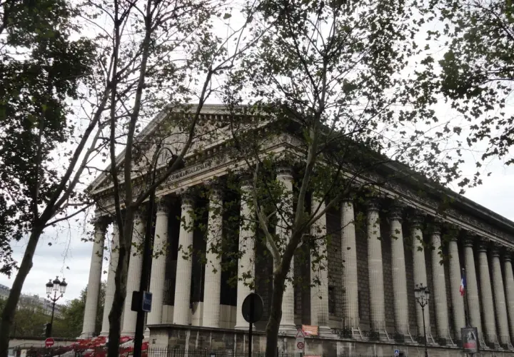 Kościół Madeleine w Paryżu z kolumnadą i drzewami na pierwszym planie.