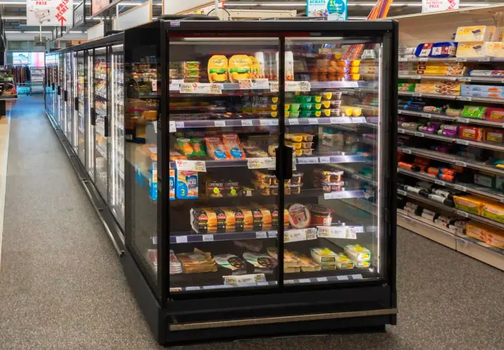 Chłodnia z produktami spożywczymi w supermarkecie, z widocznymi serami, wędlinami i deserami.