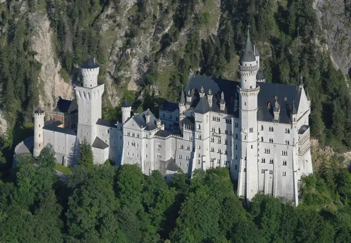 Bajkowy zamek w Niemczech, Neuschwanstein, wyrasta z zielonych lasów na tle skalistego zbocza.