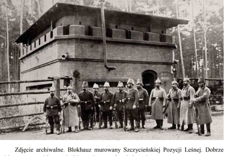 Żołnierze pozują przed murowanym blokhauzem, jednym z bunkrów Hitlera, z widocznymi stanowiskami strzeleckimi.