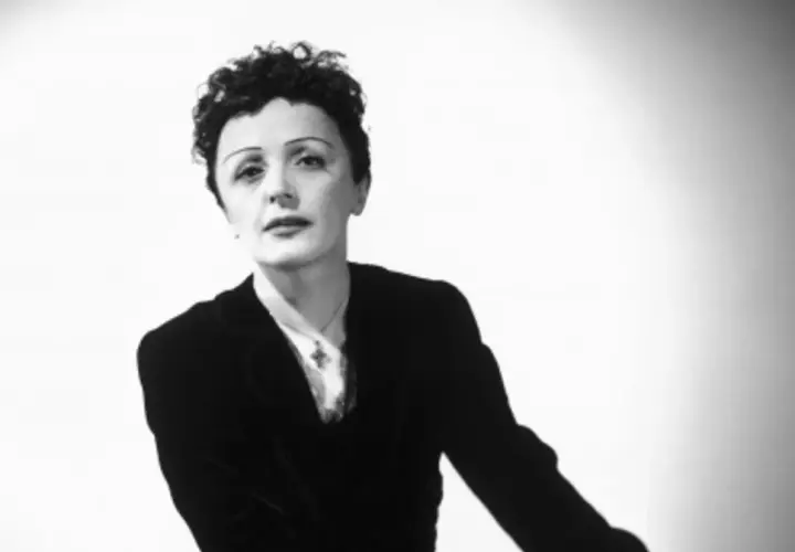 Edith Piaf w czarno-białym portrecie, w czarnym żakiecie i z charakterystyczną fryzurą.