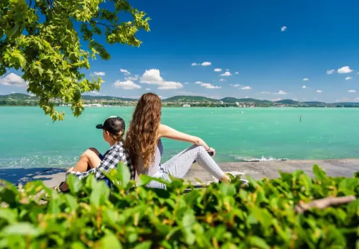 Dzieci odpoczywają na plaży Balaton, podziwiając turkusową wodę i zielone wzgórza w oddali.