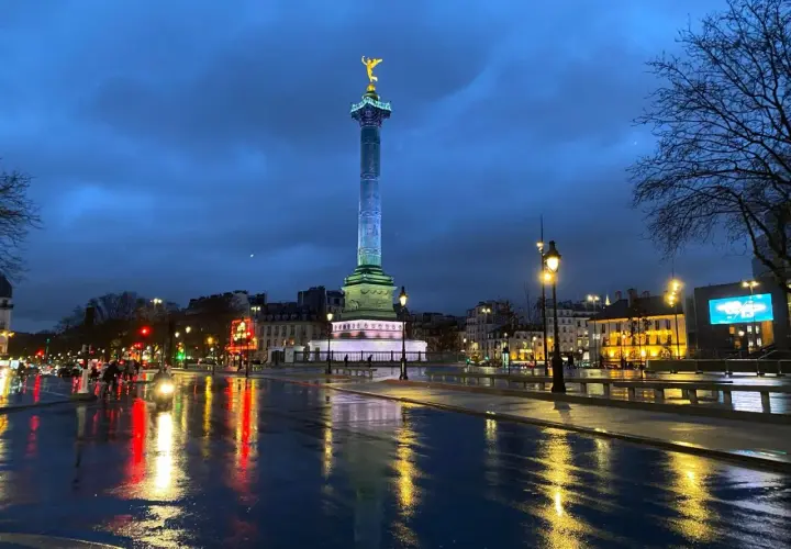 Wieczorny Paryż po deszczu. Kolumna Bastylii lśni w świetle latarni, a mokry asfalt odbija światła miasta.