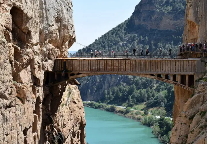 Spacerzy po wąwozie El Caminito del Rey, atrakcji, z której słynie Malaga. Widok na most nad turkusową rzeką.