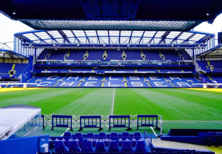 Puste trybuny stadionu Chelsea Londyn, zielona murawa i niebieskie siedzenia czekają na kibiców.