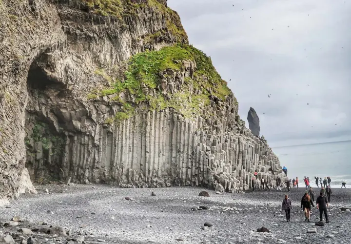 Niesamowita czarna plaża Islandia z bazaltowymi kolumnami i jaskinią. Turyści spacerują po kamieniach.