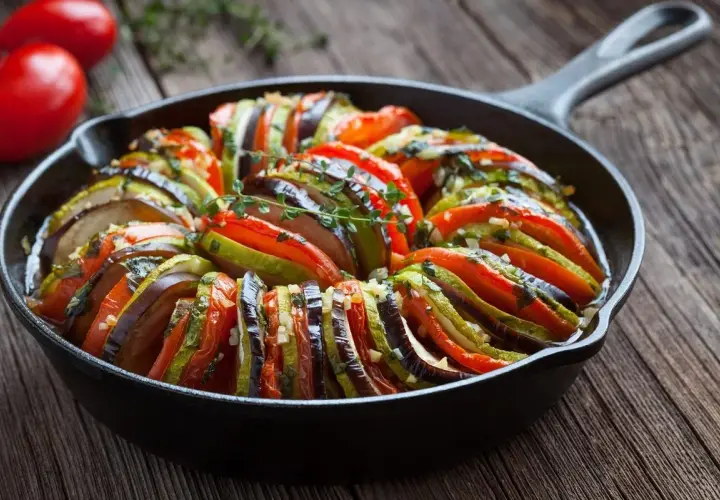 Ratatouille, jedno z popularnych dań francuskich, w naczyniu żeliwnym. Warzywa ułożone w wachlarz, ozdobione ziołami.