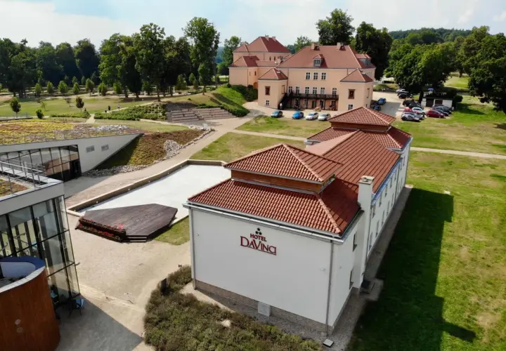 Widok z lotu ptaka na Hotel Da Vinci z czerwonym dachem, otoczony zielenią i innymi budynkami.