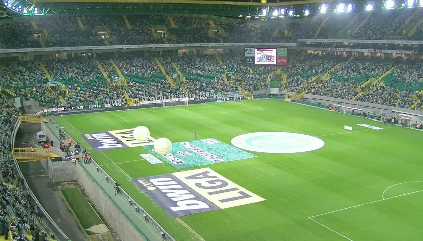 Widok na pełen widzów **sporting lizbona stadion** przed meczem. Na murawie widoczne są logotypy sponsorów i wielkie balony.