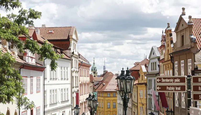 Ulica w Pradze z zabytkowymi kamienicami i latarniami. W oddali widać wieże, wskazujące na praga nietypowe atrakcje.
